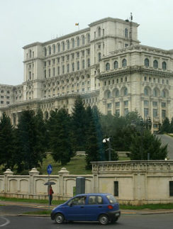 a car driving on a road next to a large white building with Palace of the Parliament in the background
