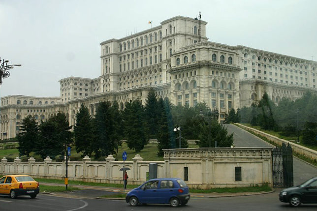 a car driving on a road next to a large white building with Palace of the Parliament in the background