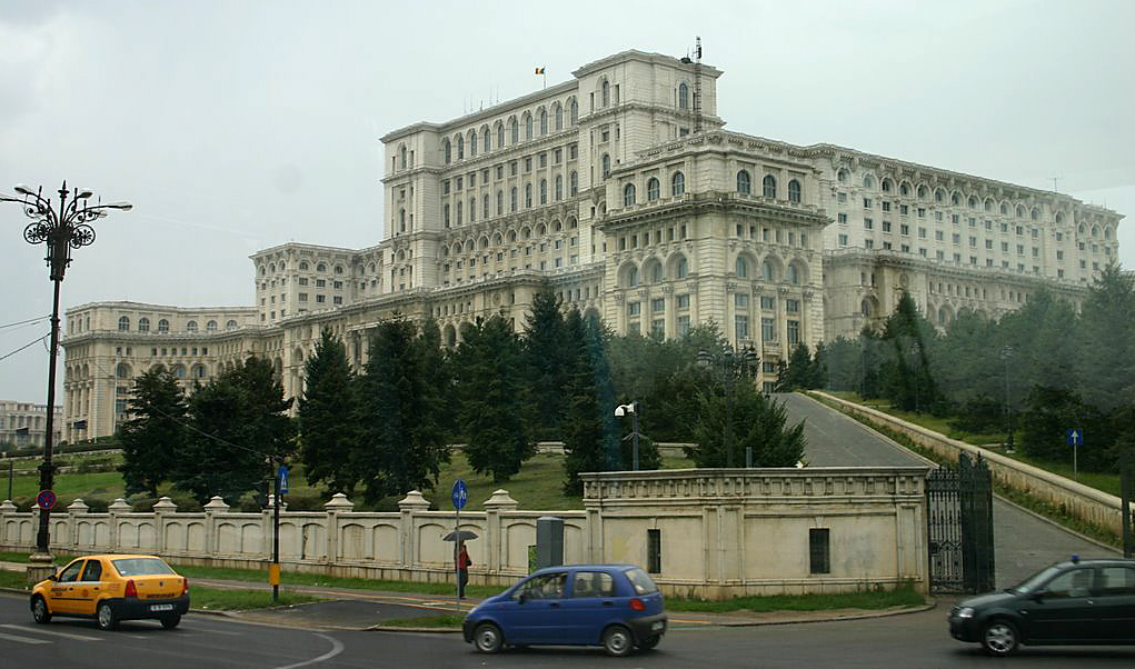 a car driving on a road next to a large white building with Palace of the Parliament in the background