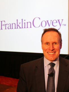 a man in a suit smiling in front of a large screen