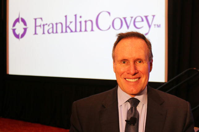 a man in a suit smiling in front of a large screen