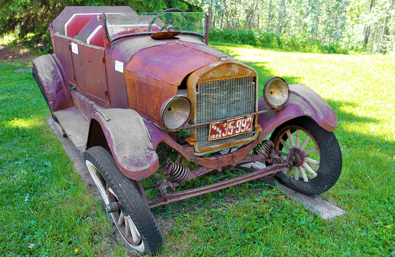 an old rusty car parked in a grassy area