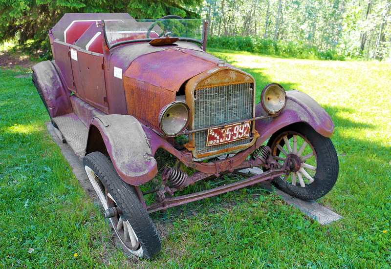 an old rusty car parked in a grassy area