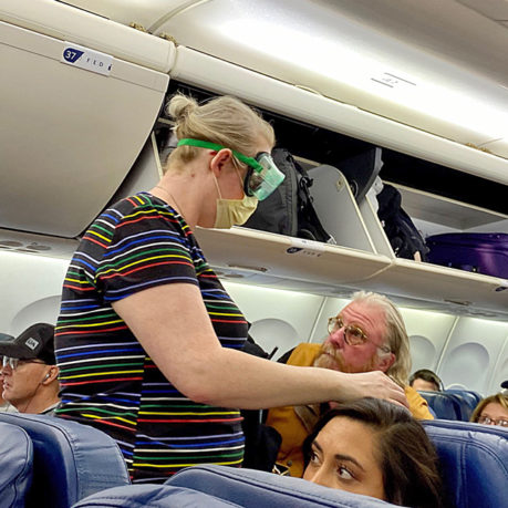 a woman in a striped shirt and mask standing in an airplane