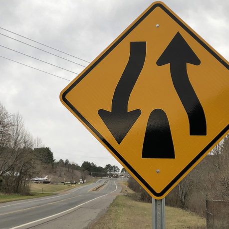 a yellow road sign with arrows pointing to the left