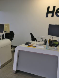 a two white desks with computers and a black sign on the wall