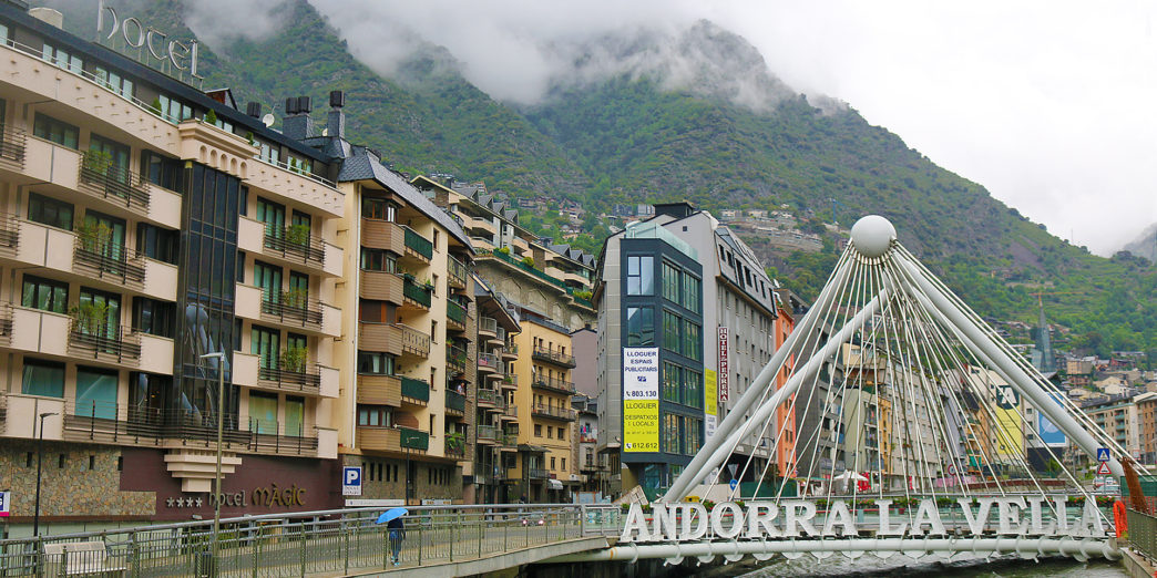 a bridge over a river with buildings and mountains in the background