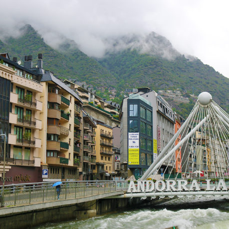 a bridge over a river with buildings and mountains in the background