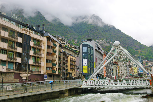a bridge over a river with buildings and mountains in the background