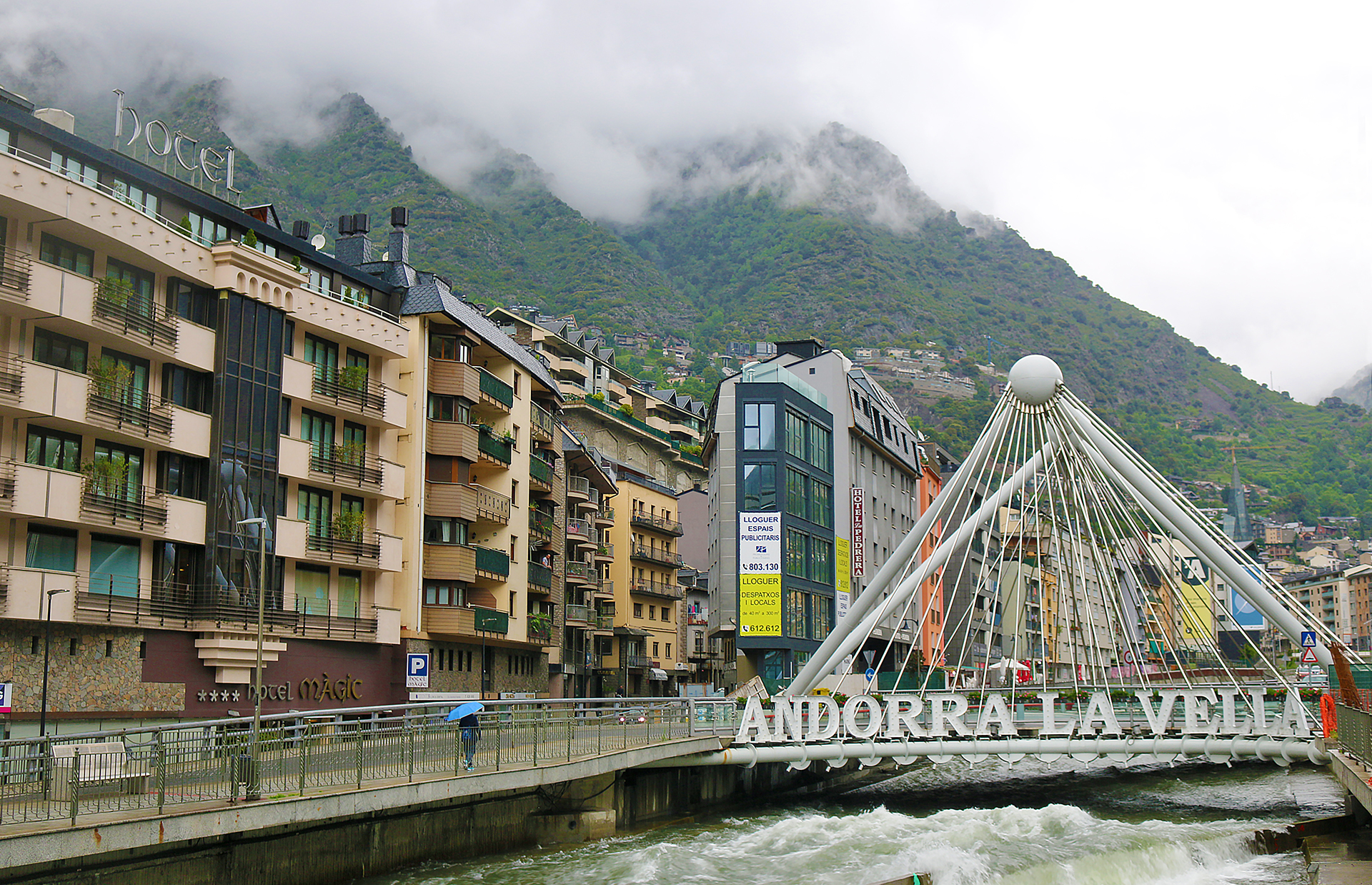 a bridge over a river with buildings and mountains in the background