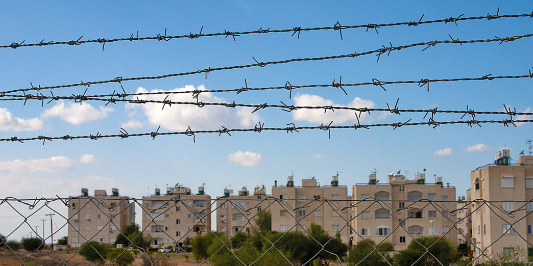 a barbed wire fence with buildings in the background