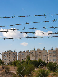 a barbed wire fence with buildings in the background