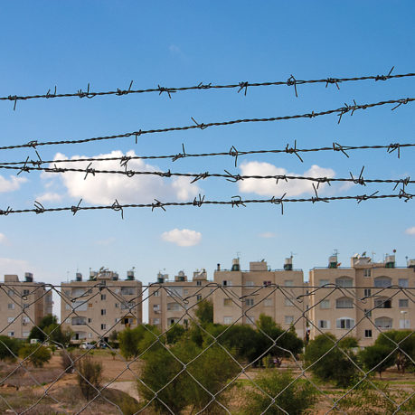 a barbed wire fence with buildings in the background