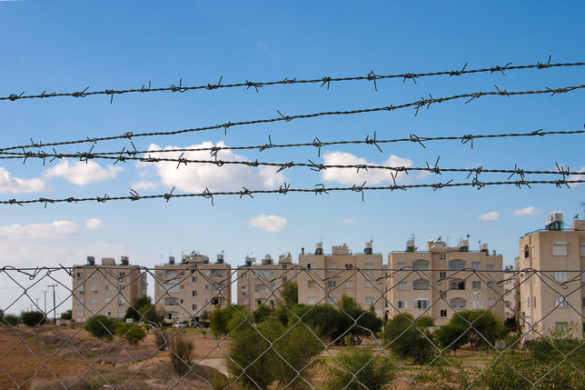 a barbed wire fence with buildings in the background