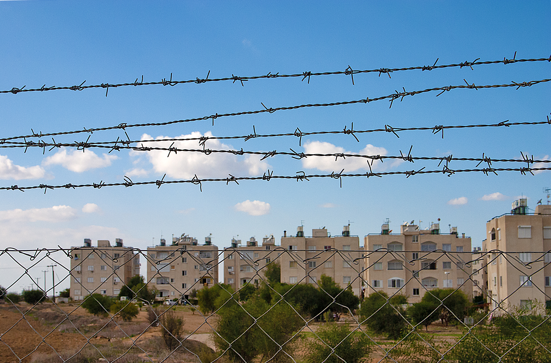 a barbed wire fence with buildings in the background