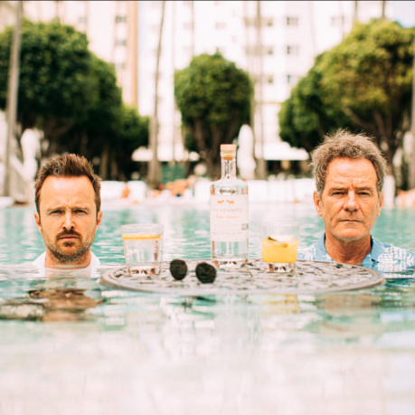 two men in a pool with drinks and a table