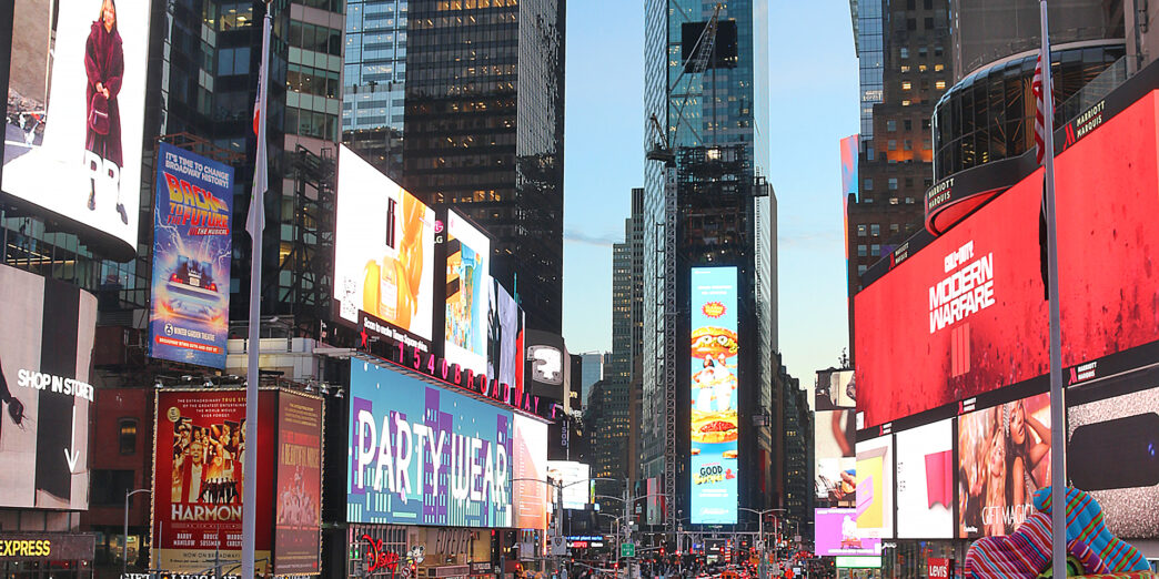 a large crowd of people in a busy city street with Times Square in the background