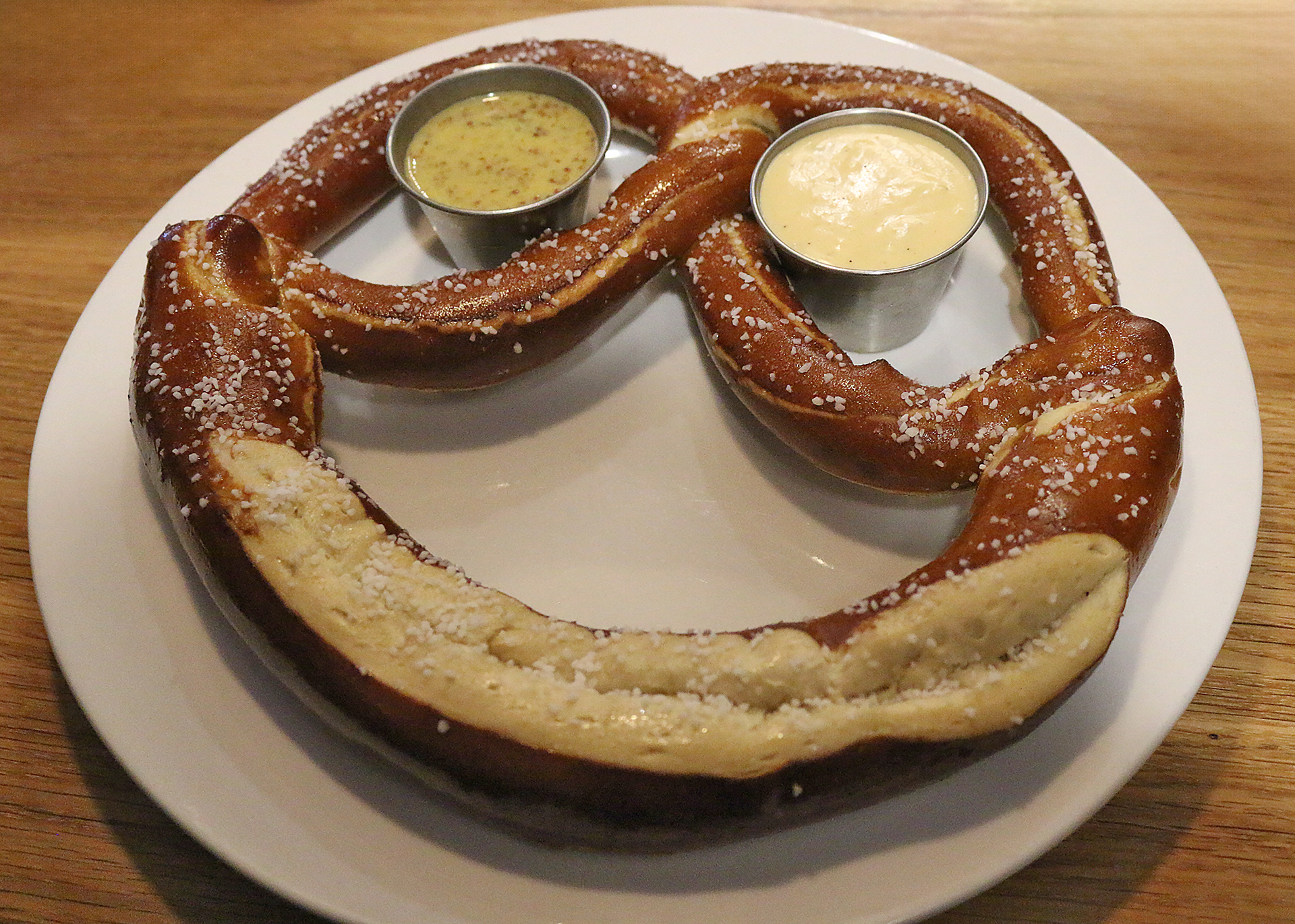 a pretzel with two small cups of sauce on a white plate