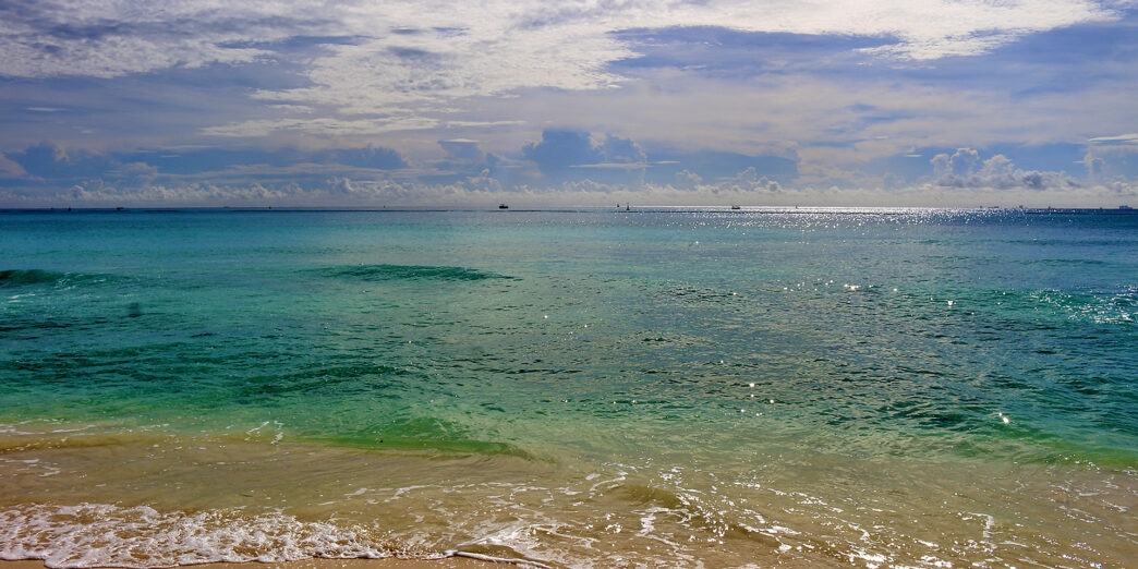a beach with blue water and clouds