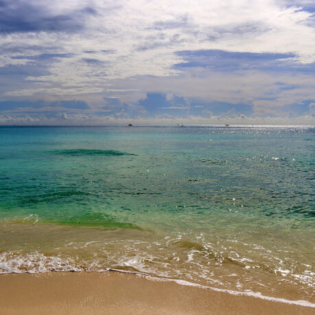 a beach with blue water and clouds