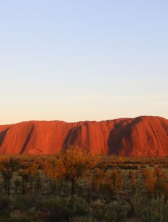 a large red rock in the desert with Uluru in the background