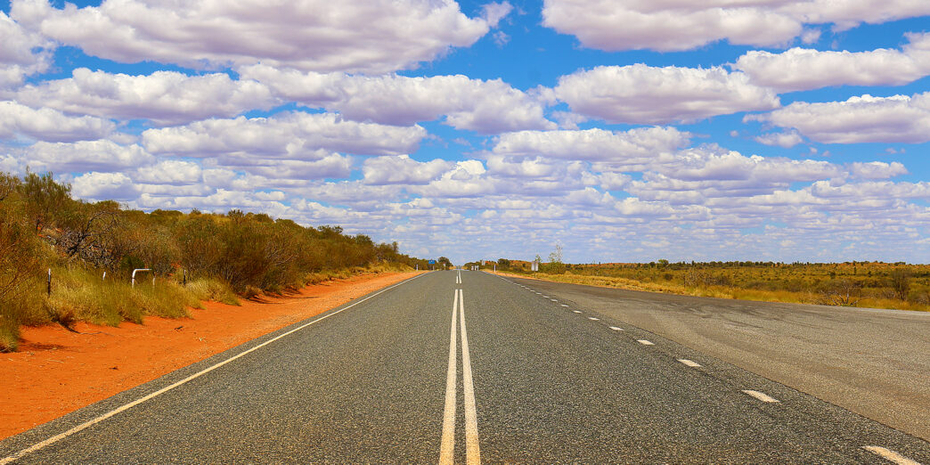 a road with a white line on the side with Nullarbor Plain in the background