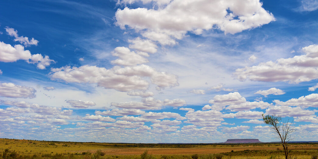 a landscape with a large field and blue sky with clouds
