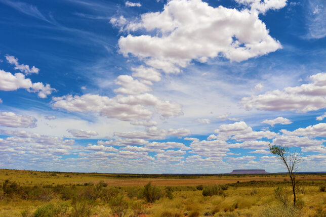 a landscape with a large field and blue sky with clouds