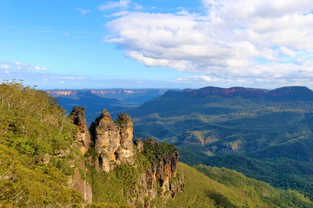a rocky cliff with trees and mountains in the background
