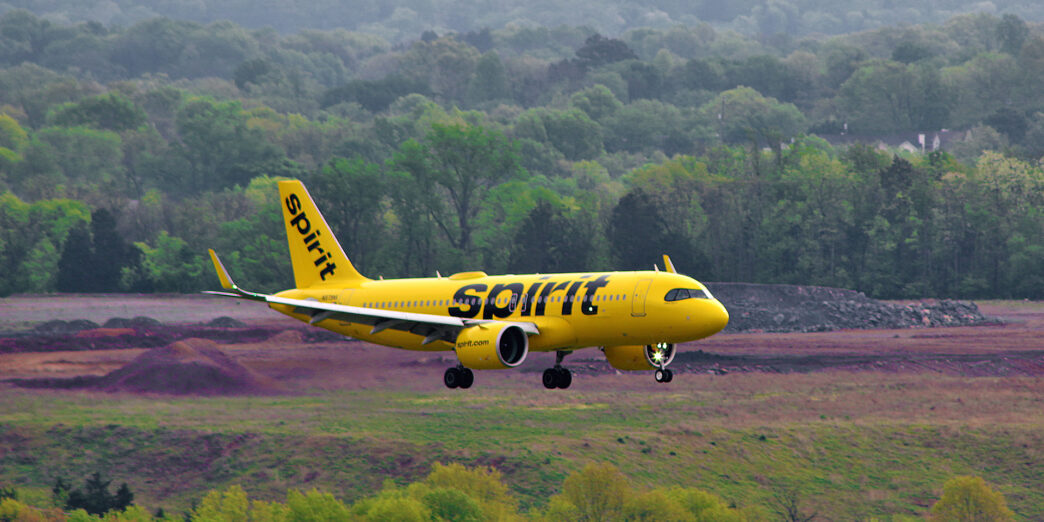 a yellow airplane flying over a field with trees