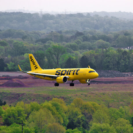 a yellow airplane flying over a field with trees