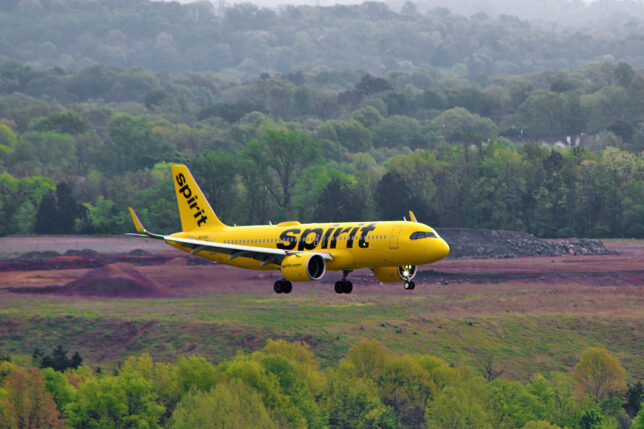 a yellow airplane flying over a field with trees