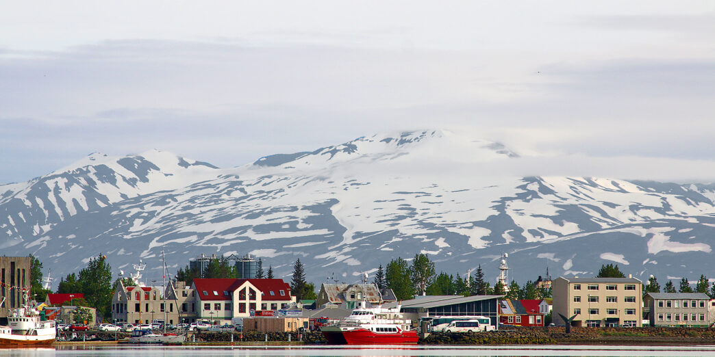 a city next to water with snow covered mountains in the background