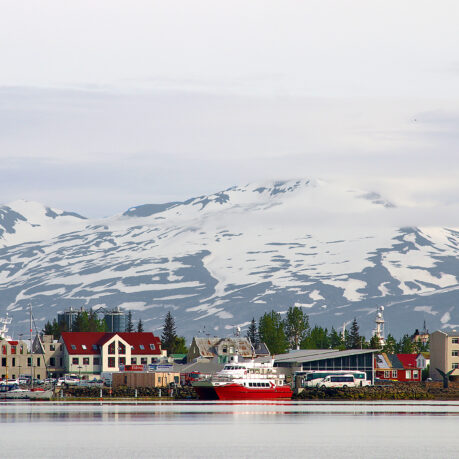 a city next to water with snow covered mountains in the background