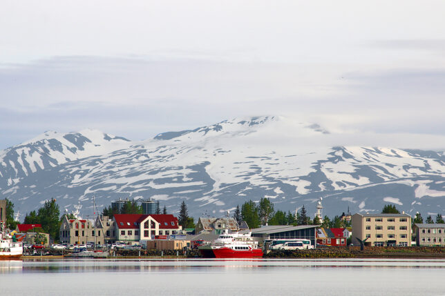 a city next to water with snow covered mountains in the background