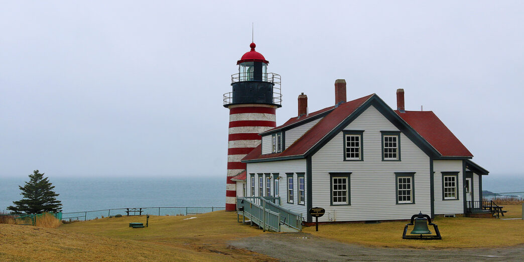 a lighthouse next to a body of water with West Quoddy Head Light in the background