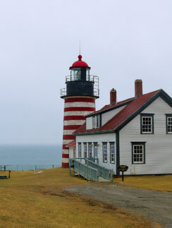 a lighthouse next to a body of water with West Quoddy Head Light in the background