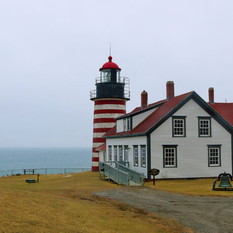 a lighthouse next to a body of water with West Quoddy Head Light in the background