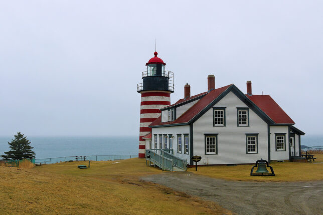 a lighthouse next to a body of water with West Quoddy Head Light in the background