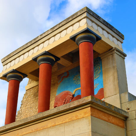 a stone building with columns and a mural on the wall with Knossos in the background