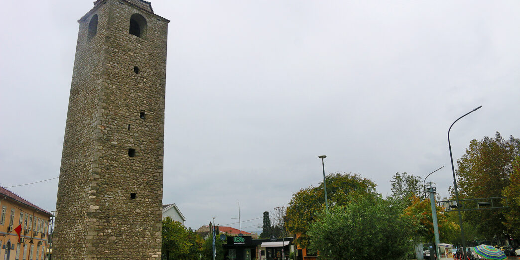 a tall stone tower with a clock tower in the middle of a park