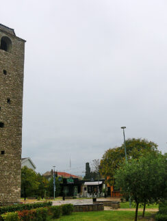 a tall stone tower with a clock tower in the middle of a park