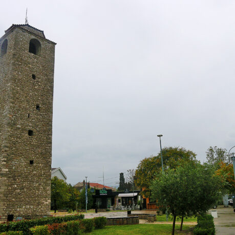 a tall stone tower with a clock tower in the middle of a park