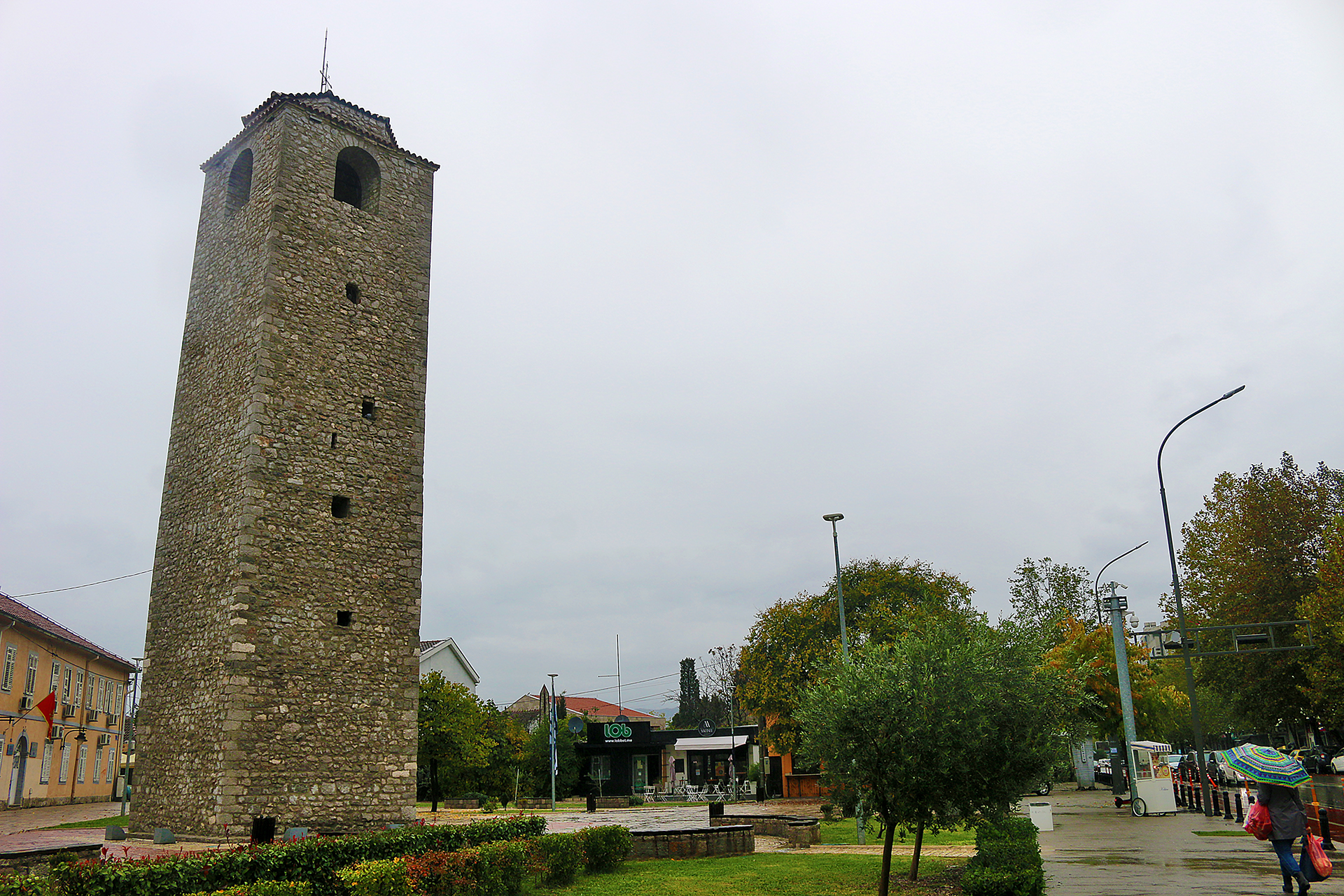 a tall stone tower with a clock tower in the middle of a park