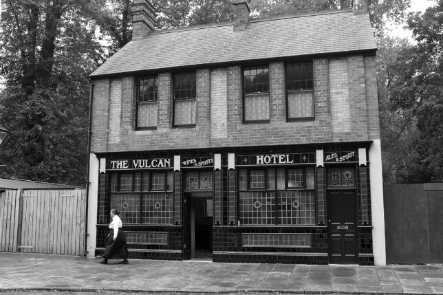 a person walking past a hotel with 251 Menlove Avenue in the background