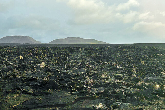 a large flat field with rocky hills in the background