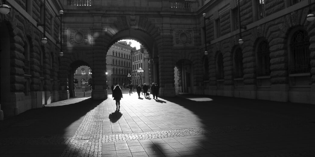 people walking under a stone archway