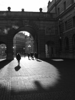 people walking under a stone archway