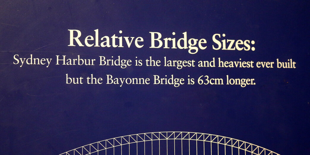a blue sign with white text and a bridge