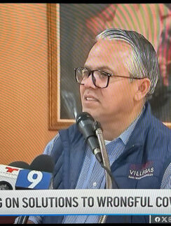 a man in glasses sitting at a podium with microphones